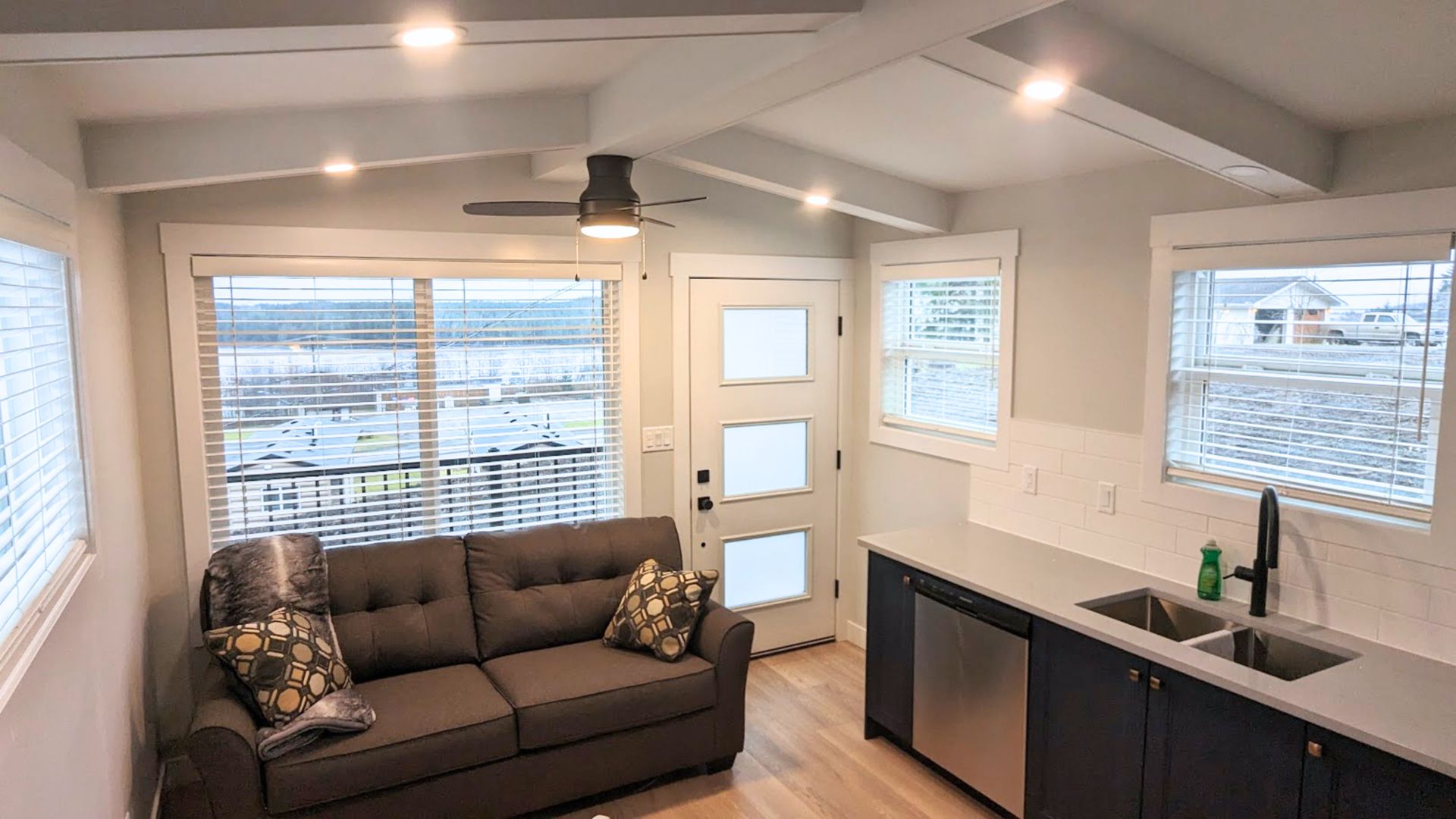 Bright modern living room with gray sofa, large windows, and a kitchen counter.