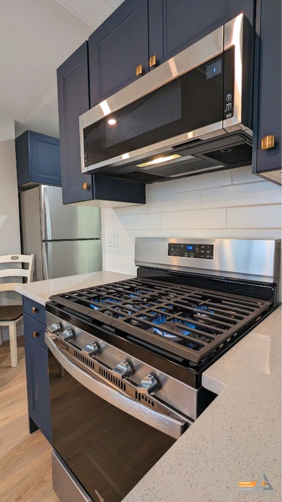 Modern kitchen with stainless steel gas range, oven, microwave, dark cabinets, and white tile backsplash