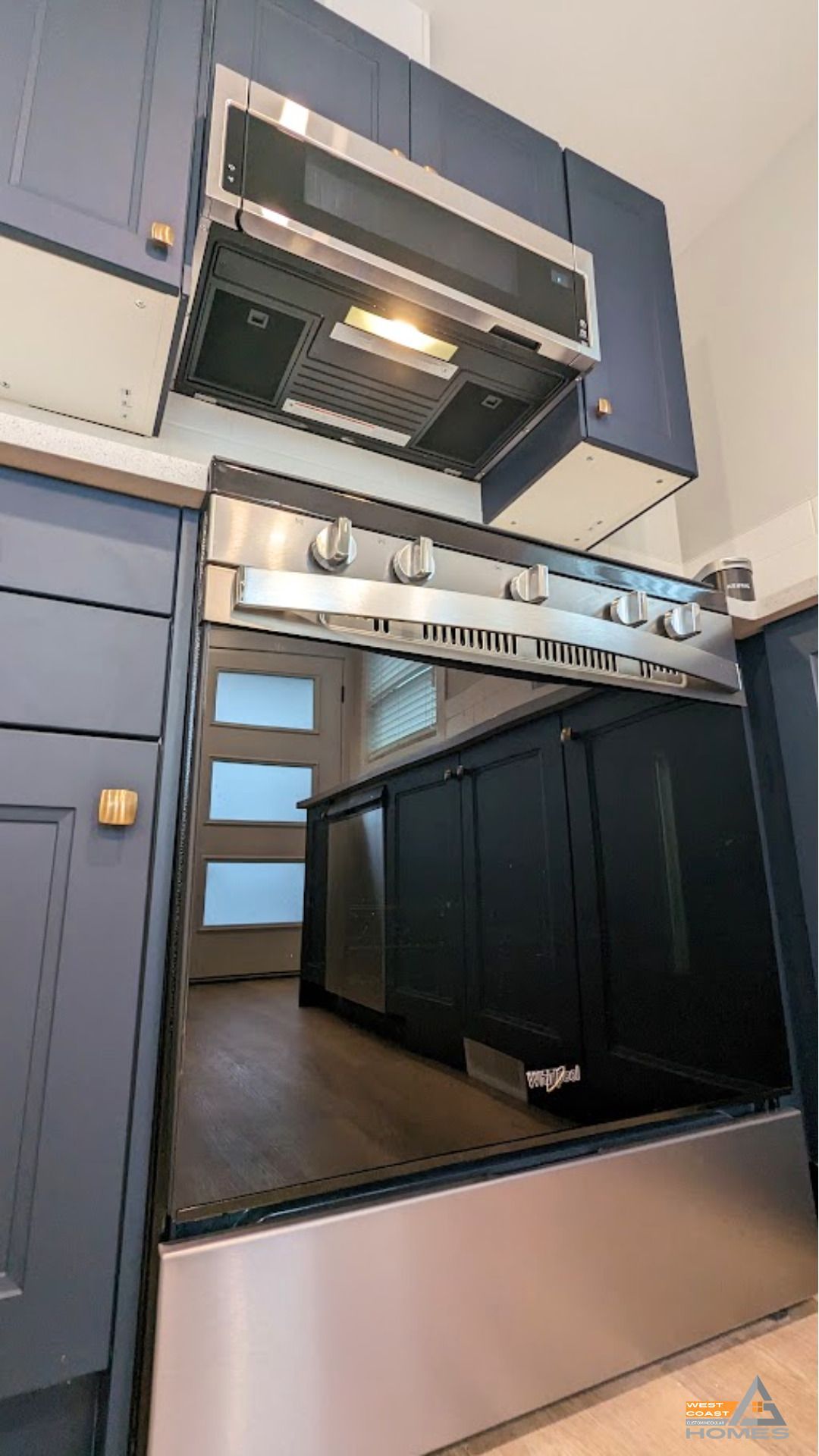 Compact modern kitchen with blue cabinets, dark countertops, and a stainless-steel stove hood under a skylight.
