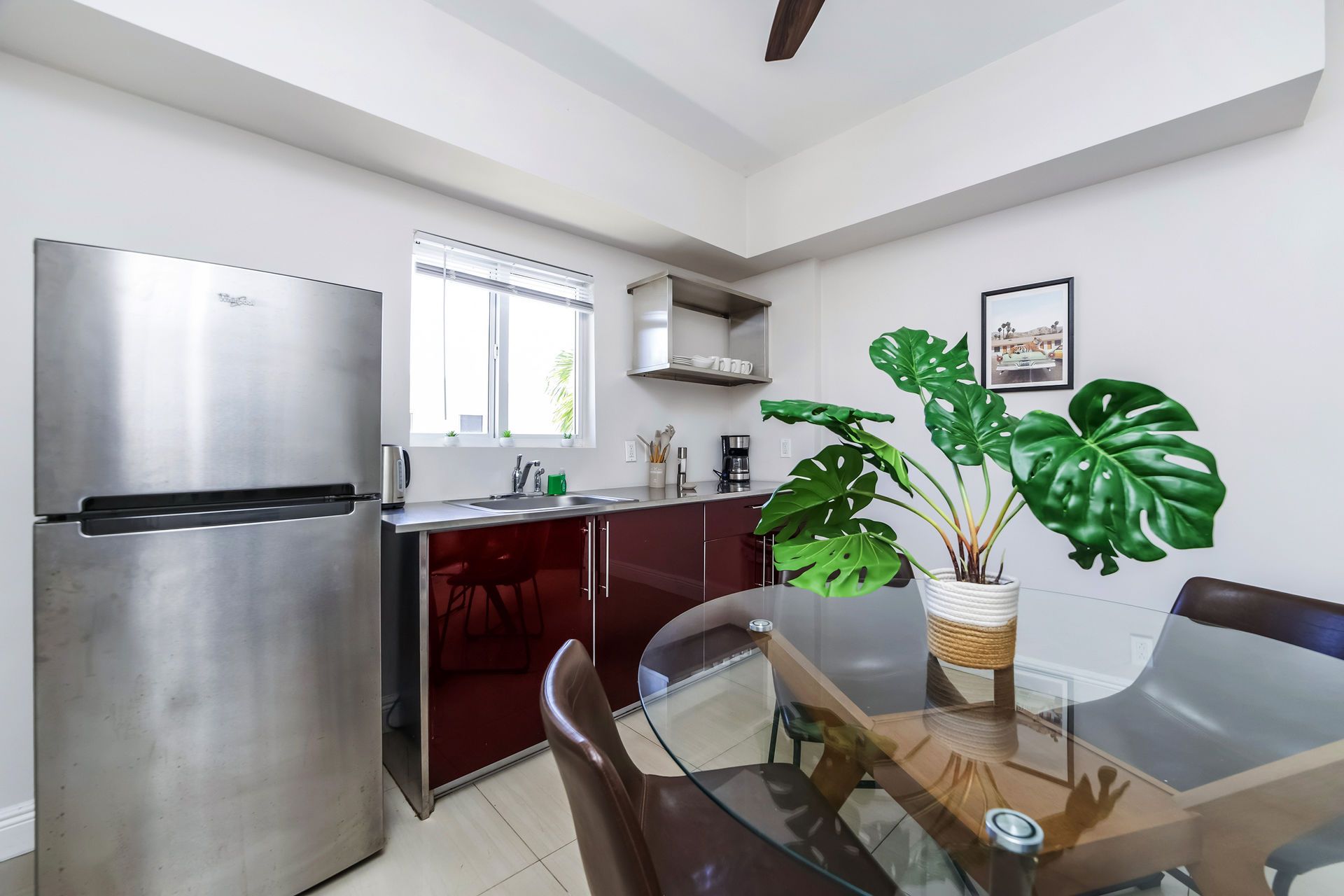 Kitchen with stainless steel fridge, red cabinets, glass dining table, and large potted plant.