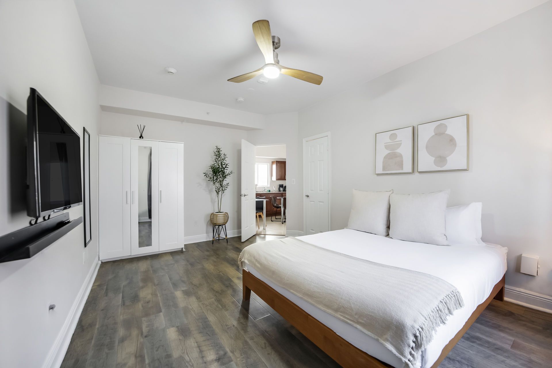 Bedroom with bed, closet, and mounted TV. Neutral color scheme, wood floors, and ceiling fan.