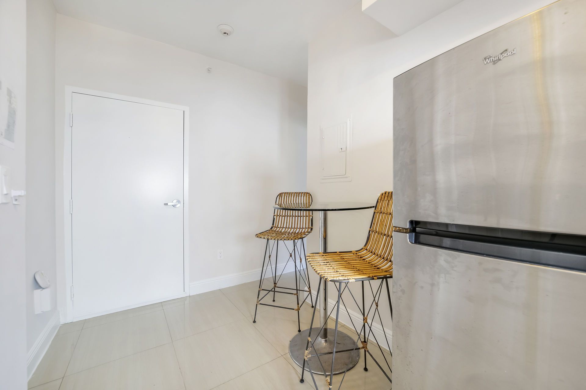Kitchen area with a stainless steel refrigerator, small table, and two bar stools.