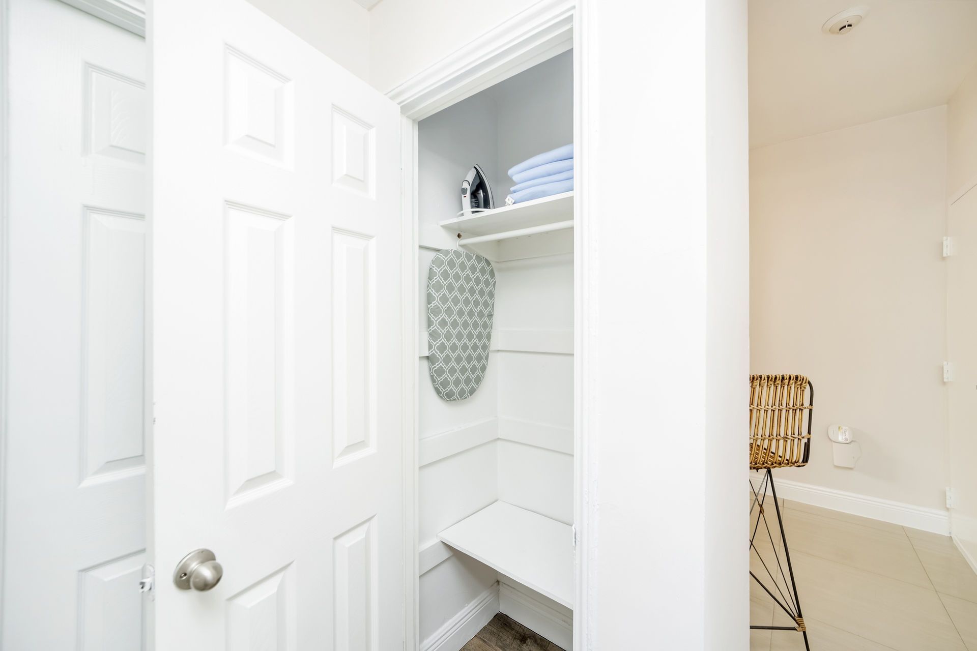 White laundry closet with ironing board, towels, and chair.