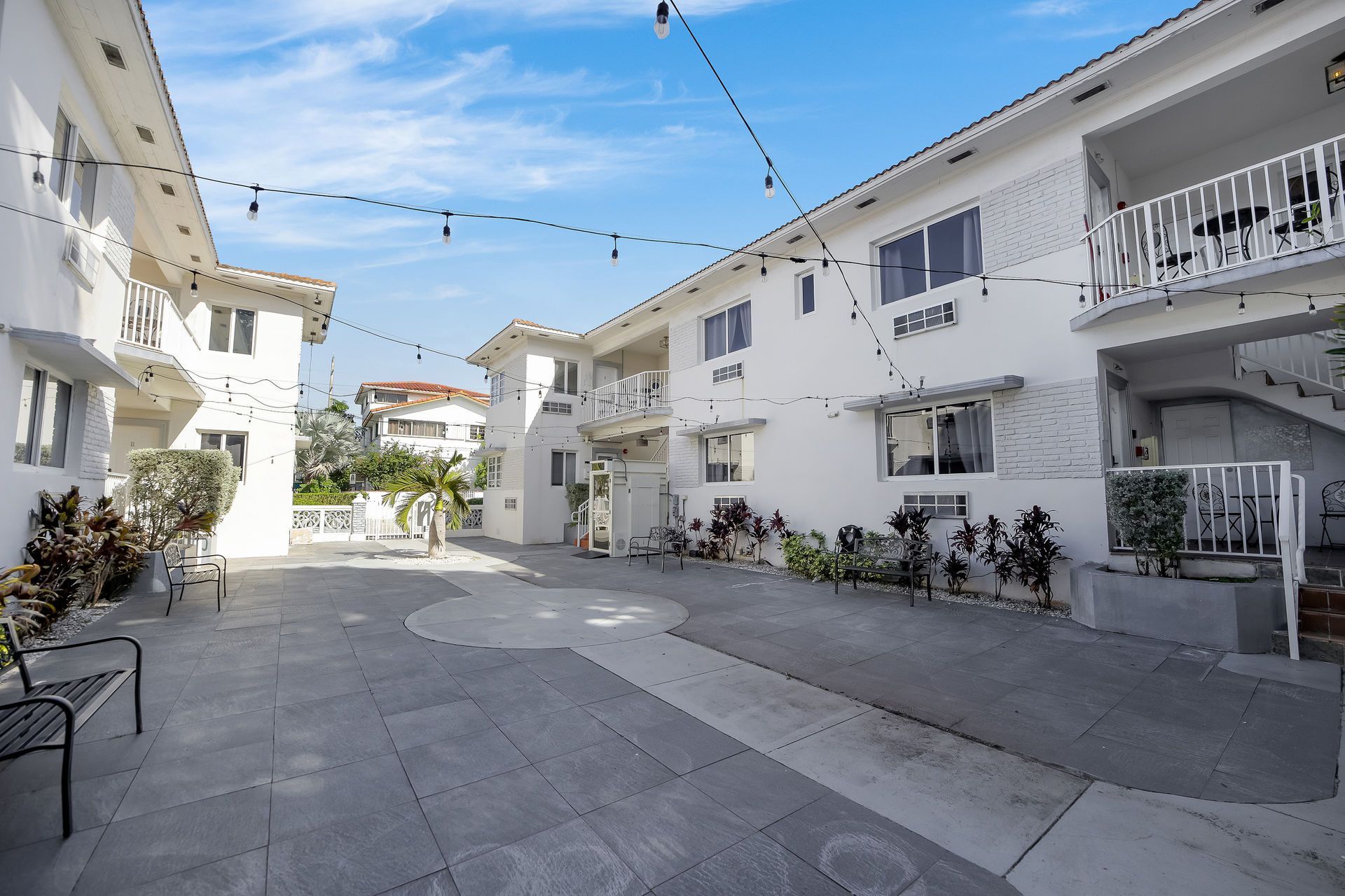 White apartment buildings with a courtyard; string lights overhead.