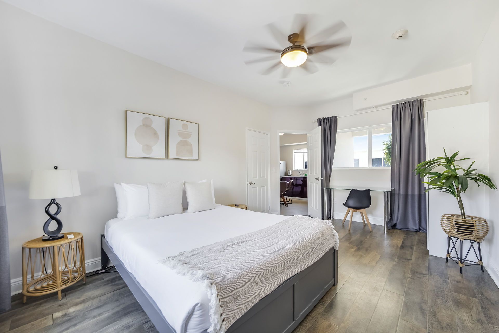 Bedroom with a gray bed, white bedding, and hardwood floors. Contains a ceiling fan, desk, and potted plant.