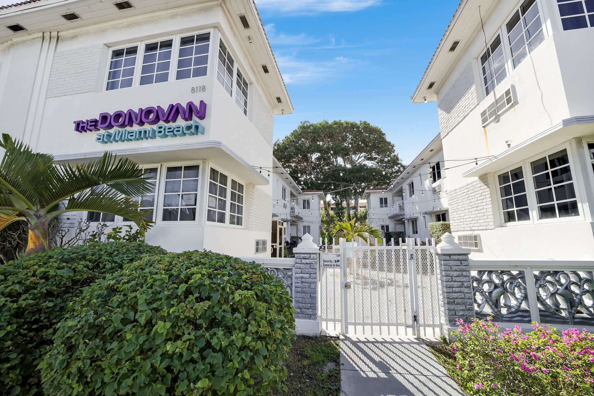 White Donovan apartment building with sign; entrance gate and greenery.