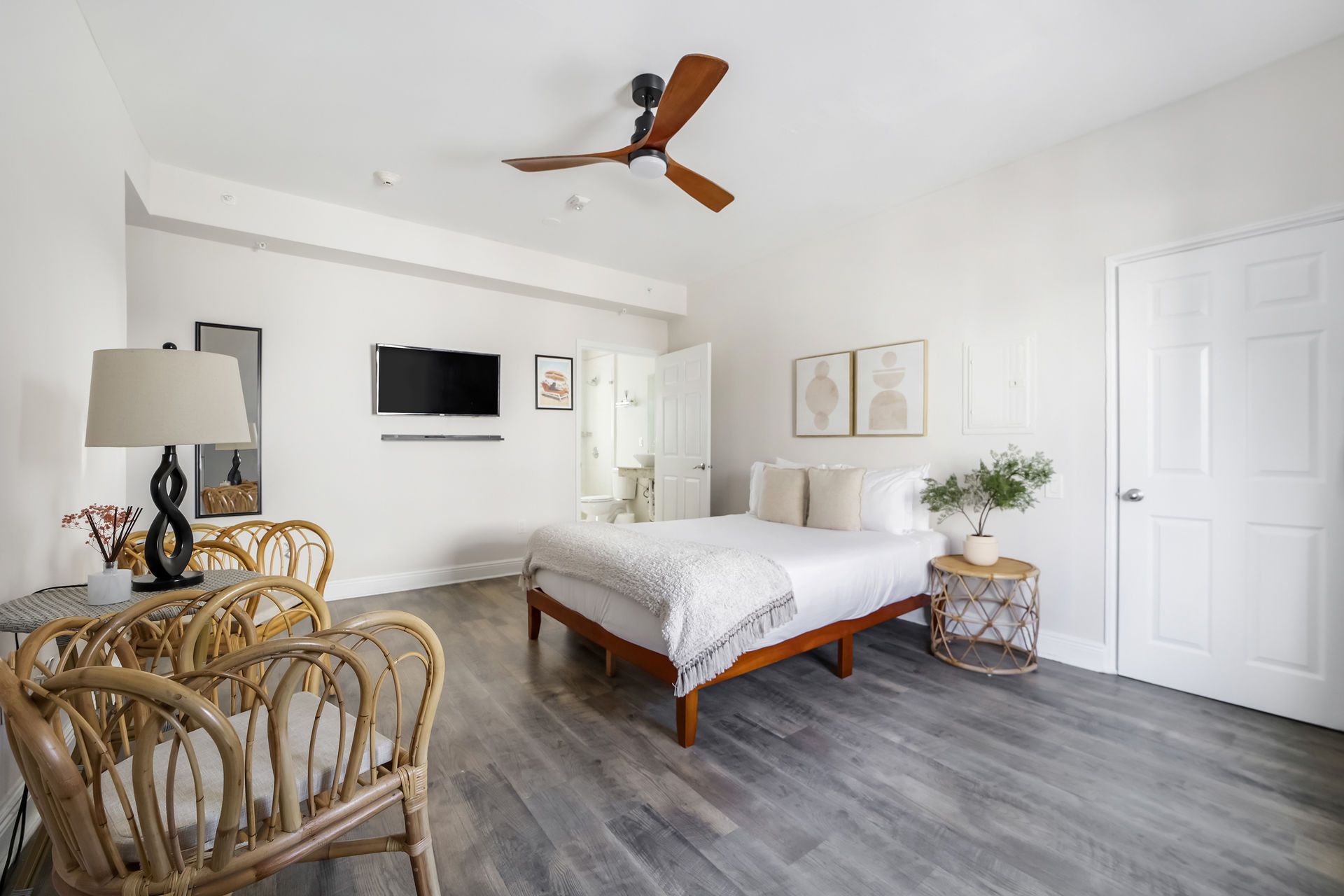 Bedroom with bed, rattan chairs, and ceiling fan; neutral tones.
