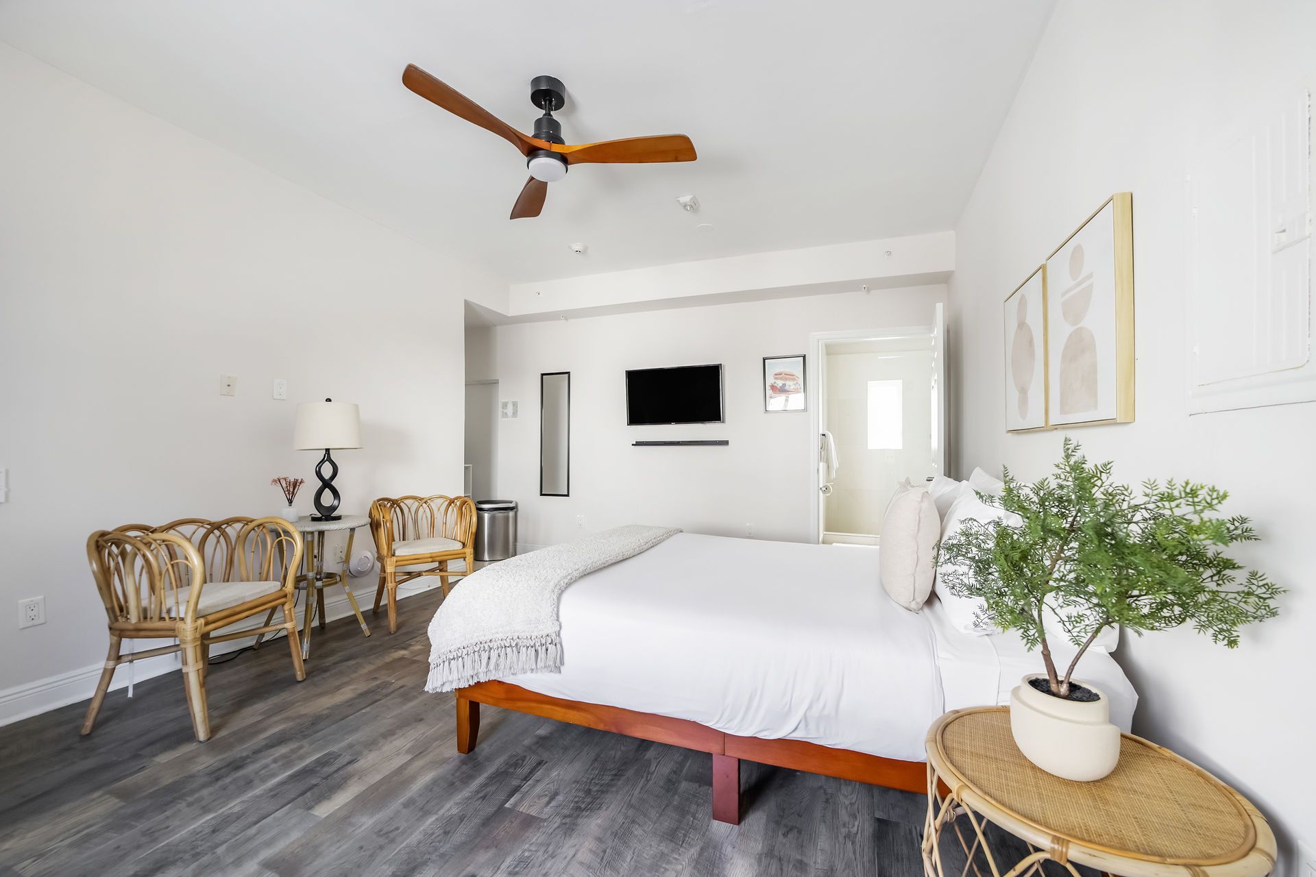 Bedroom with bed, rattan chairs, and ceiling fan; neutral tones.