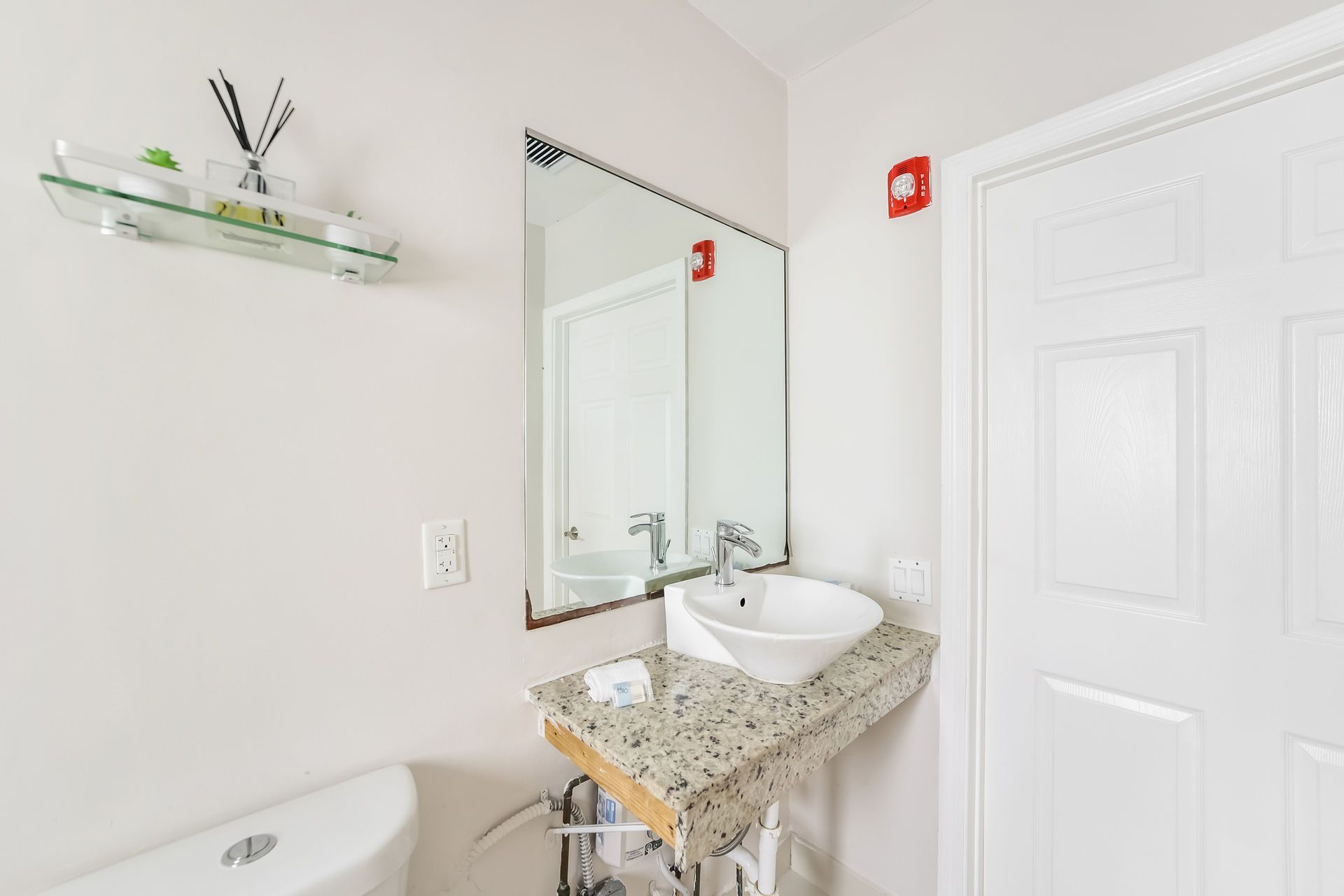 Bathroom with white sink and toilet, mirror, and a small glass shelf with items.