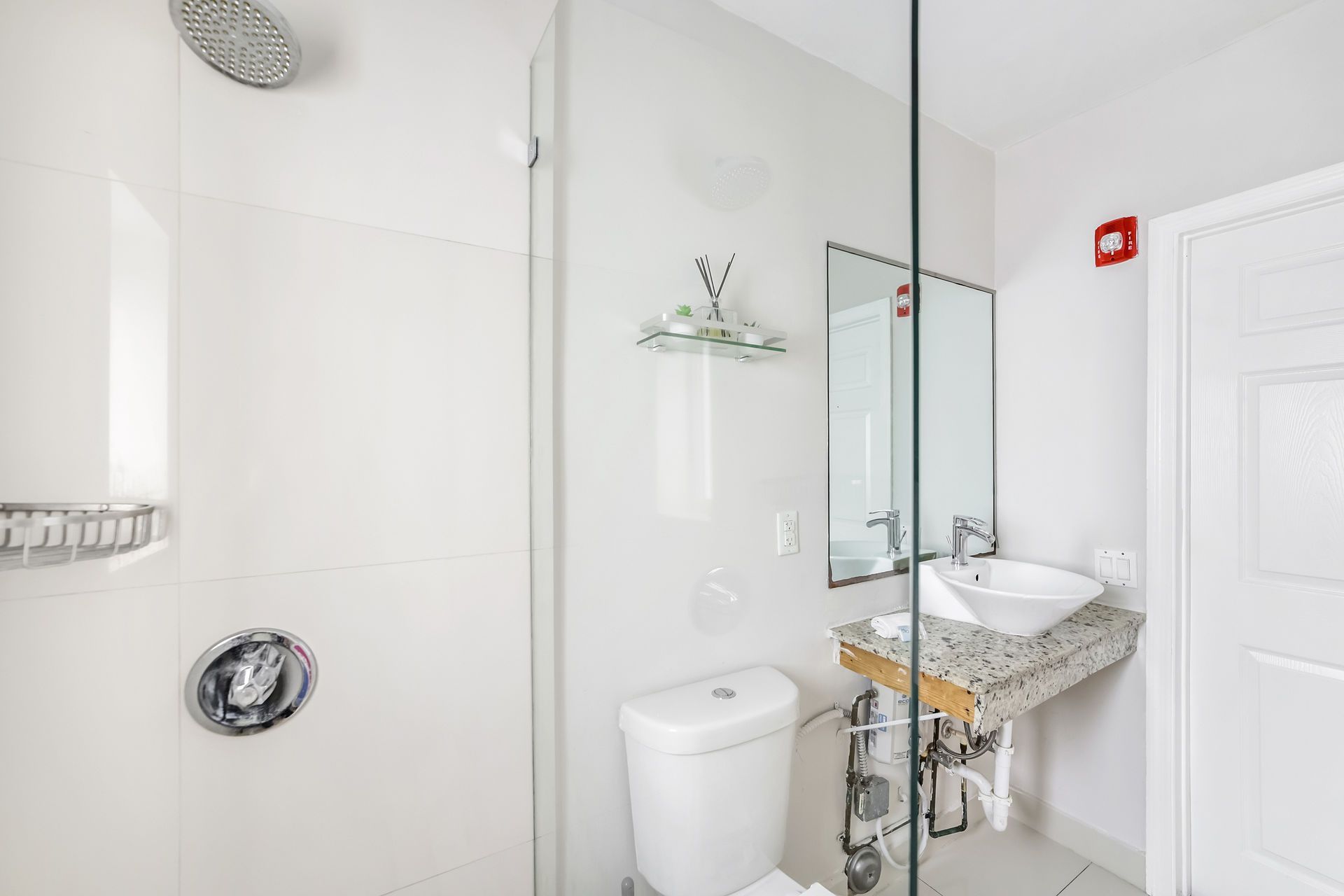 Bathroom with white walls, shower, toilet, sink, and mirror.