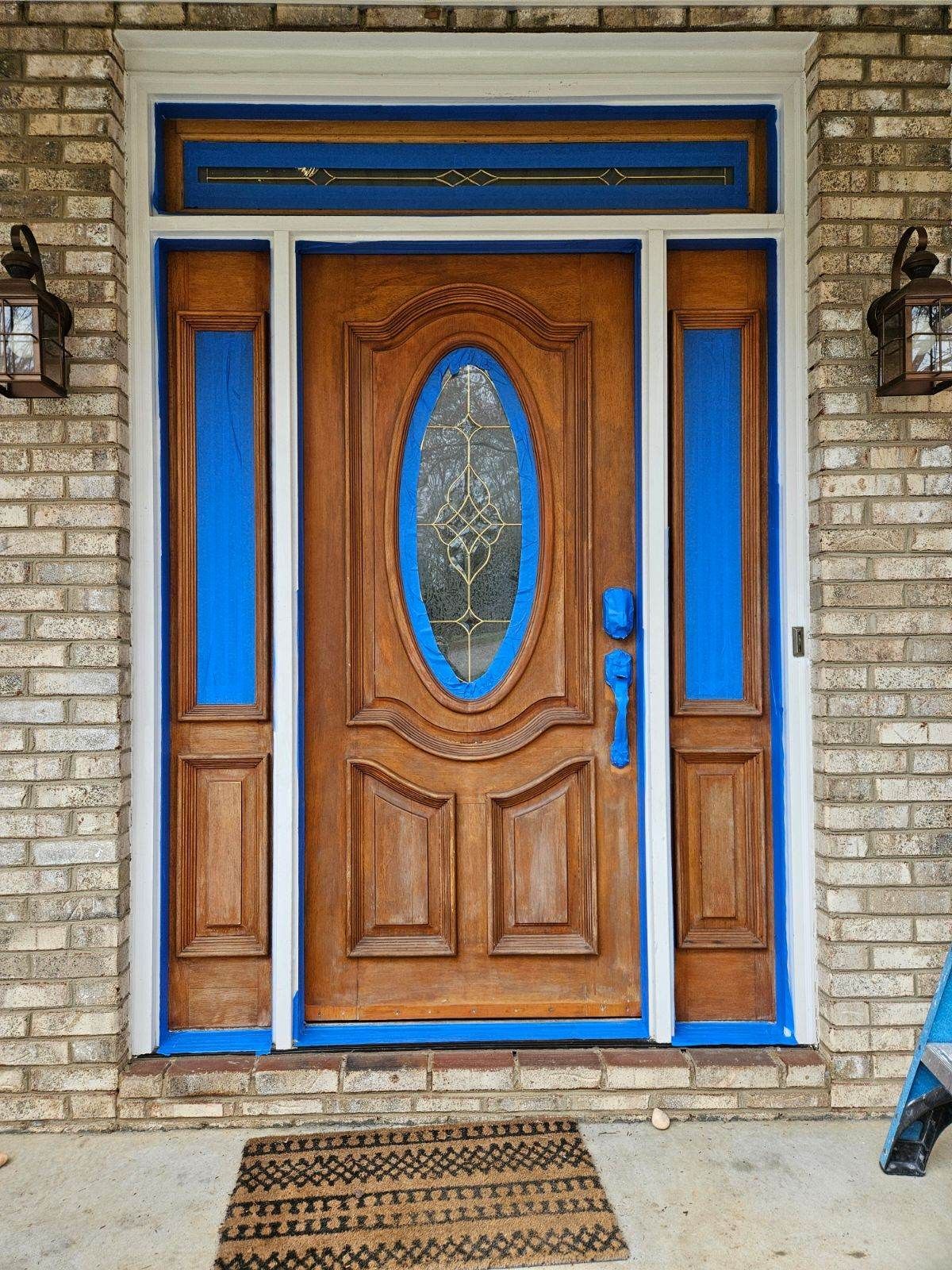Wooden front door with blue painter's tape, white trim, and a brick exterior.