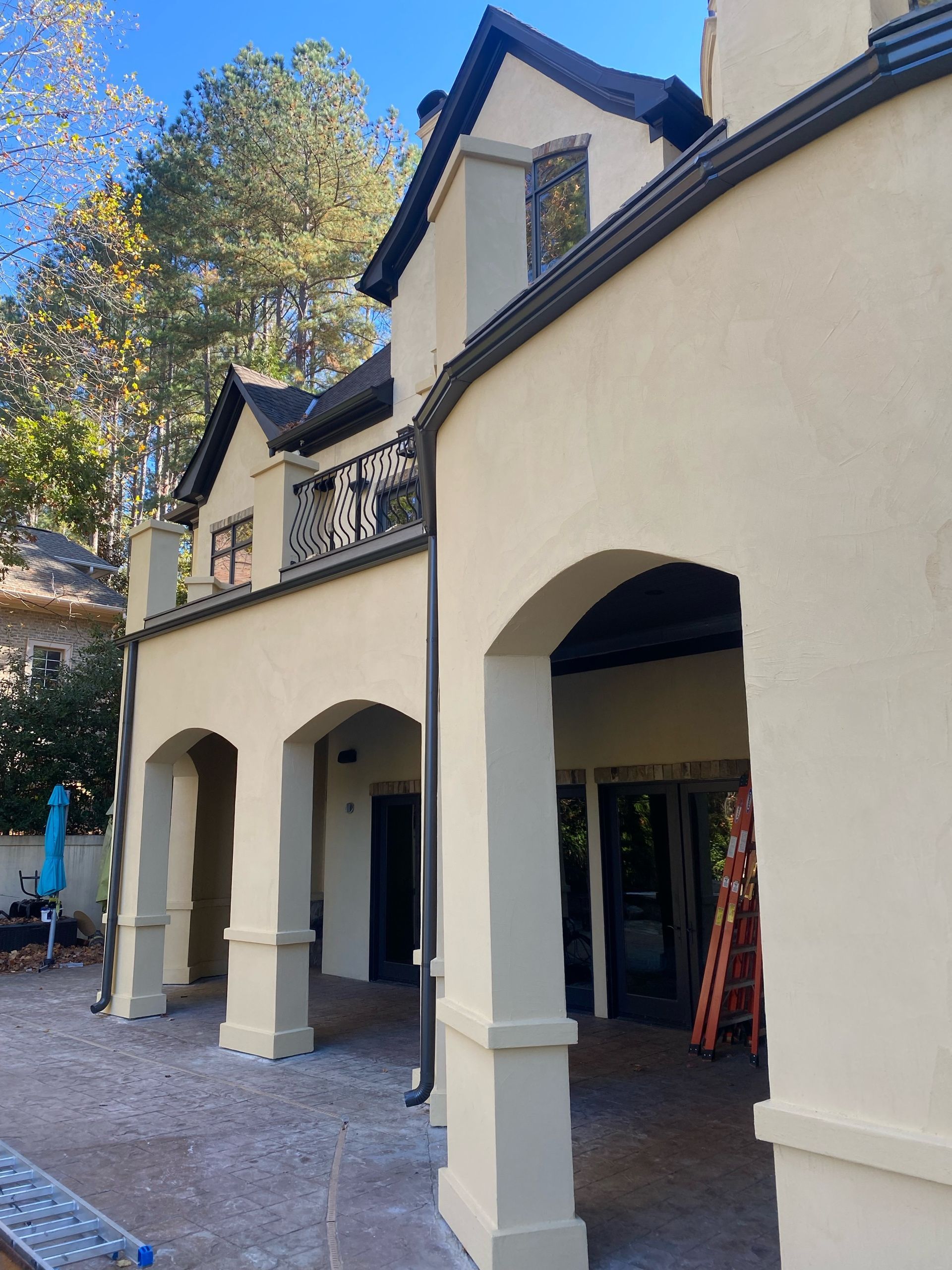 Beige stucco home with arched columns, black trim, and a balcony.