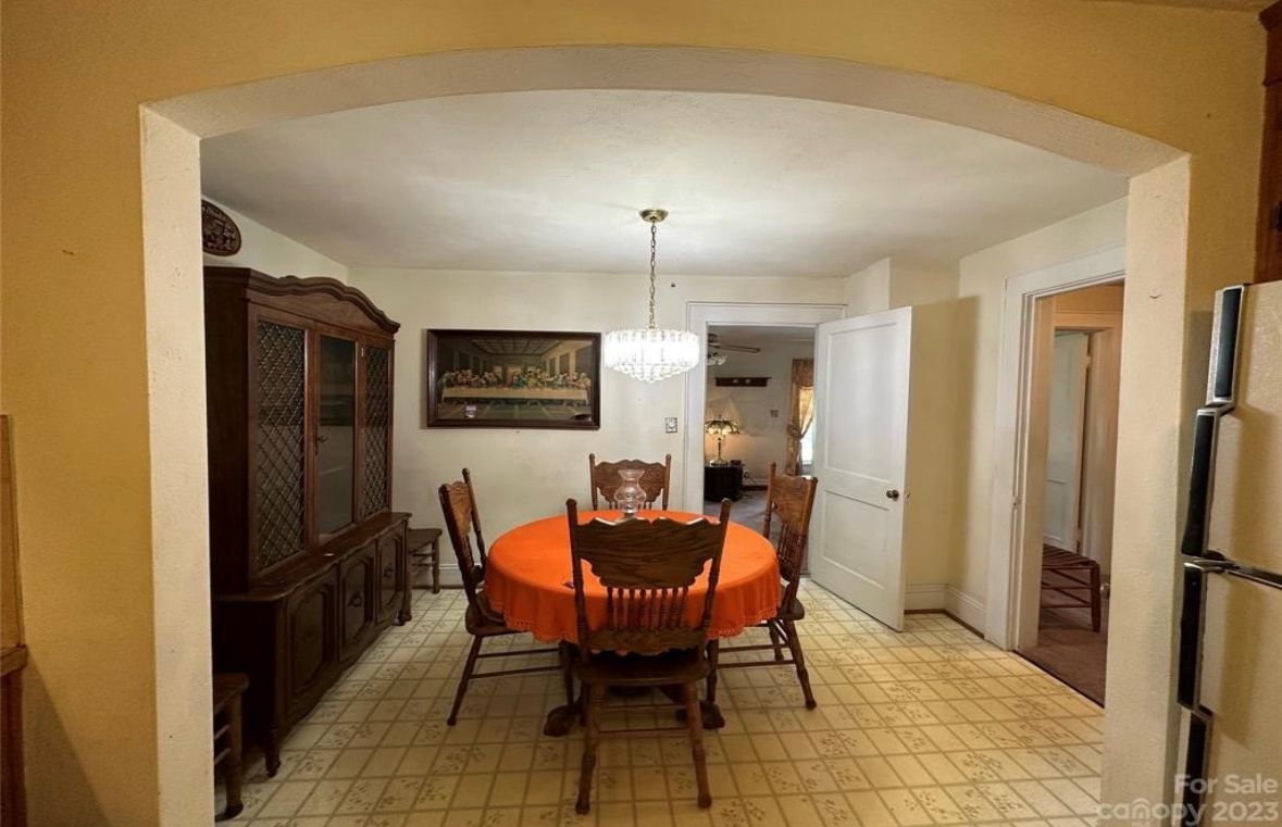 Dining room with round table, chairs, hutch, arched doorway, and chandelier.