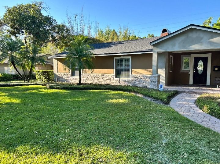 Tan house with green lawn, stone accents, palm trees, and a brick pathway.