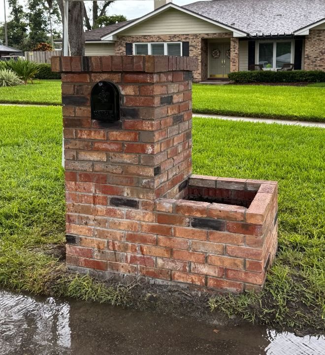 Brick mailbox with a post, fronting a grassy lawn and house.