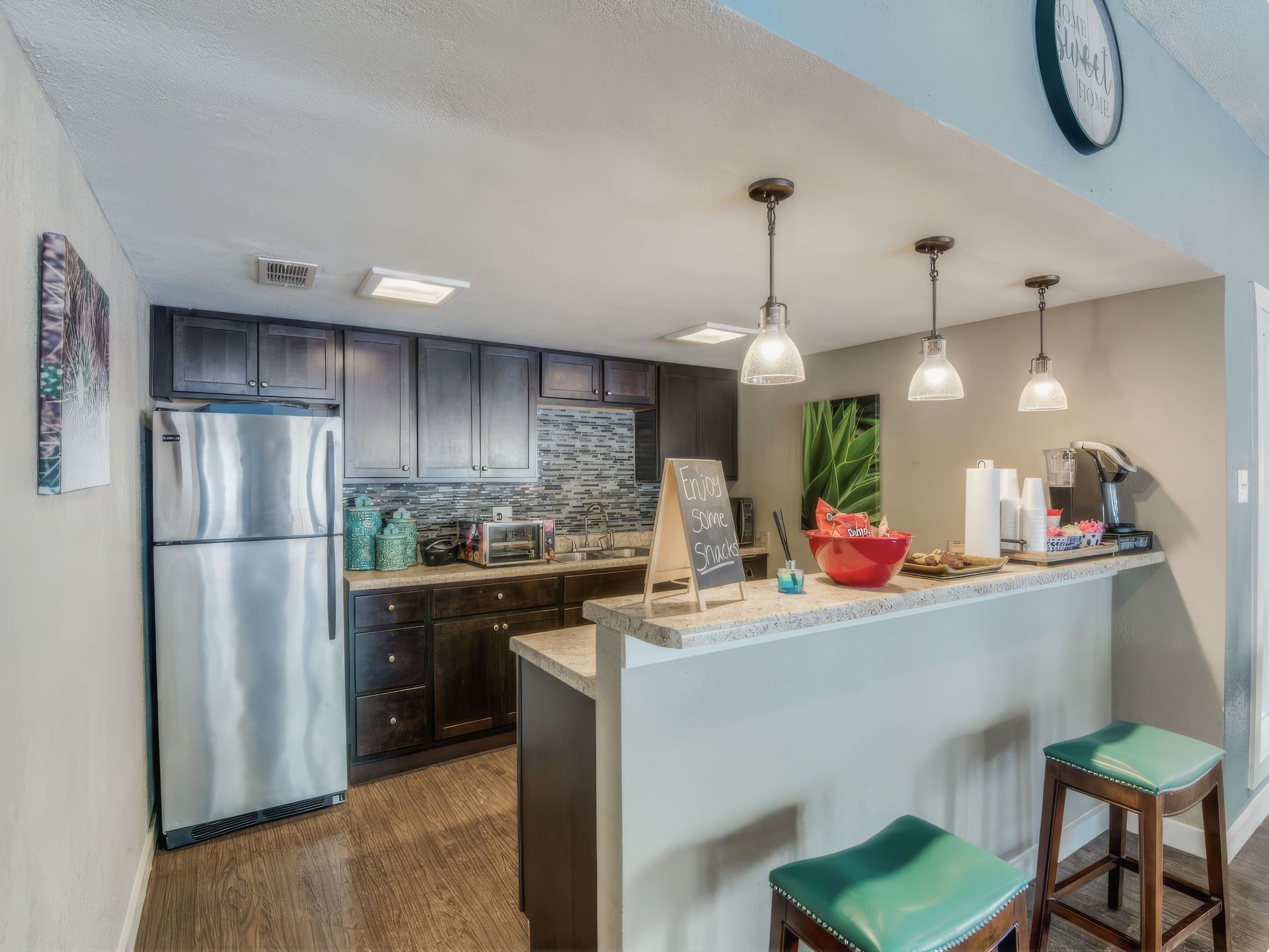 Bright kitchen with stainless fridge, island with stools, pendant lights, and blue ceiling and walls
