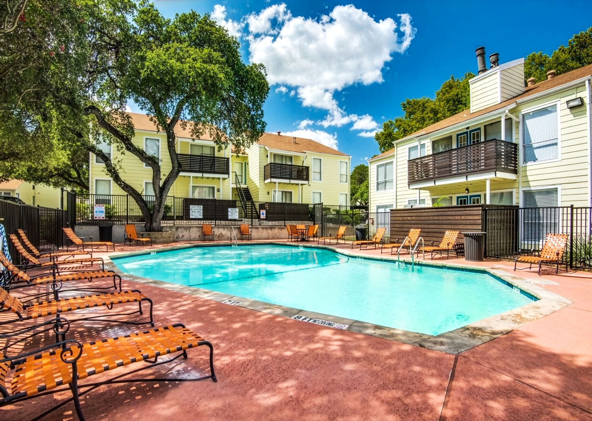 Apartment courtyard with a swimming pool, lounge chairs, and yellow buildings under a blue sky