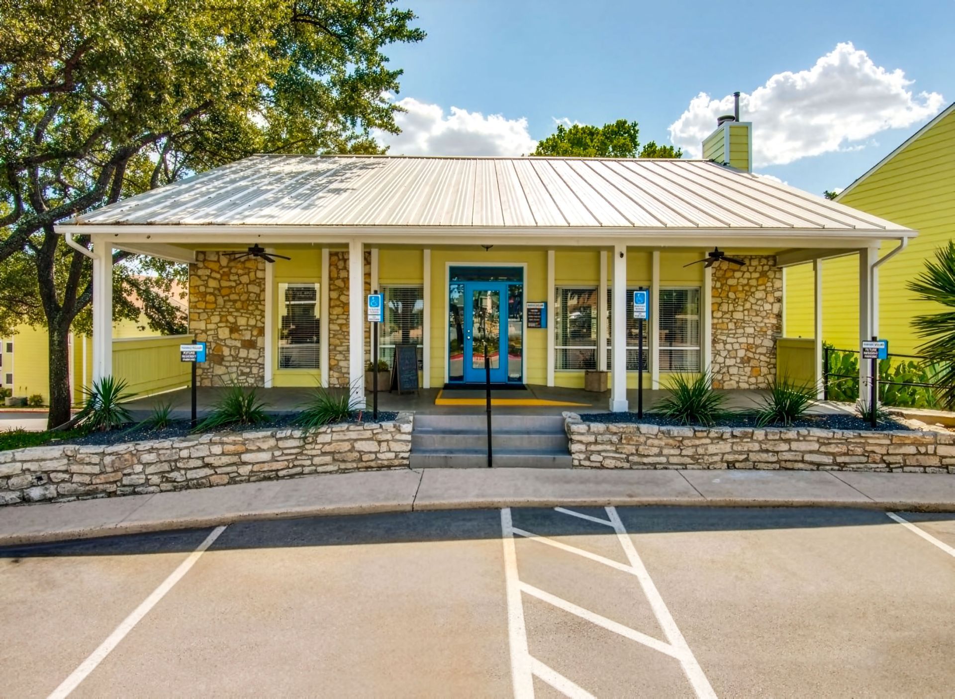 Small white building with blue doors and windows, a covered porch, and a parking lot in front