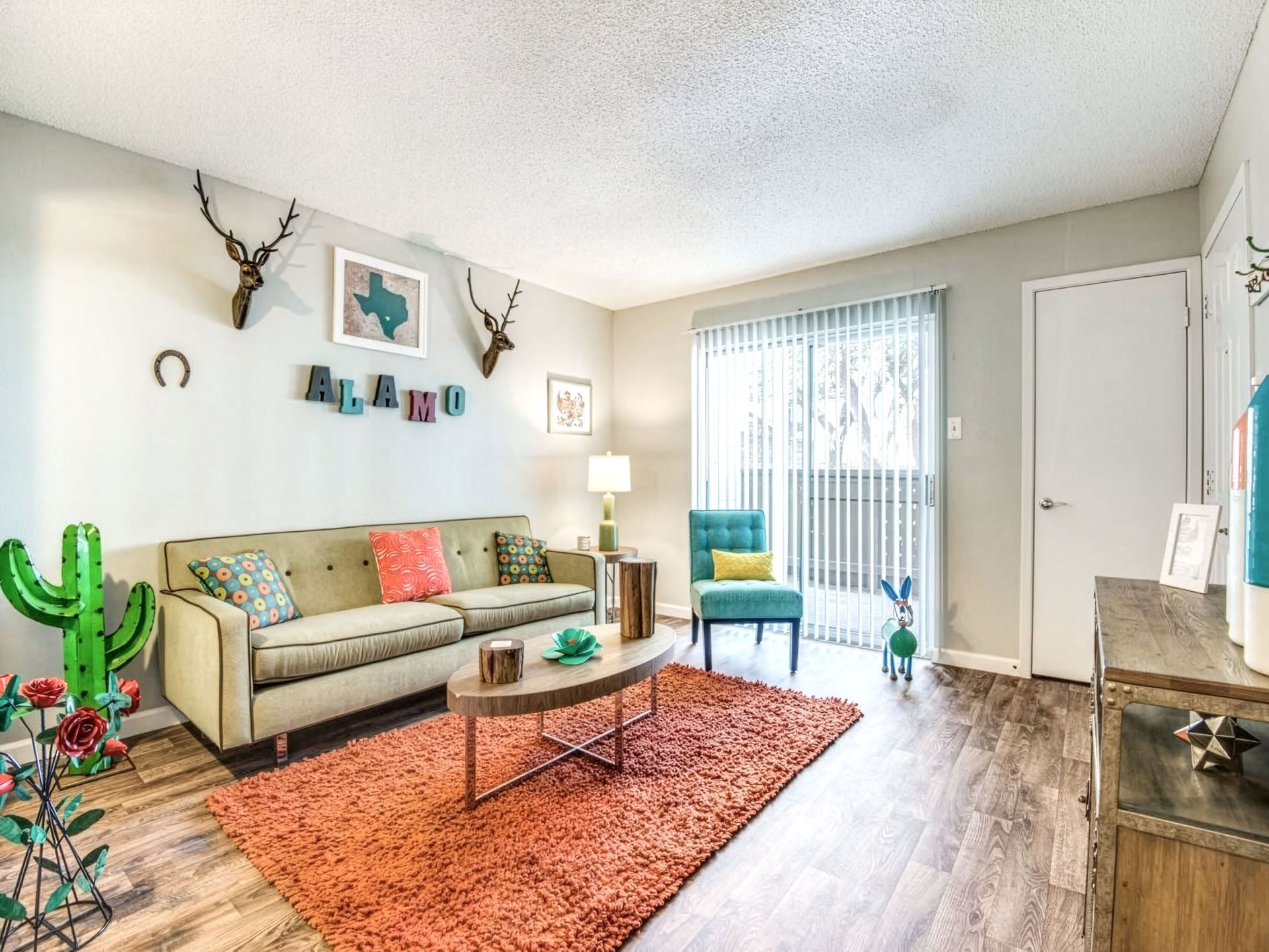 Bright living room with a beige sofa, coral rug, wood coffee table, and sliding glass door to balcony.