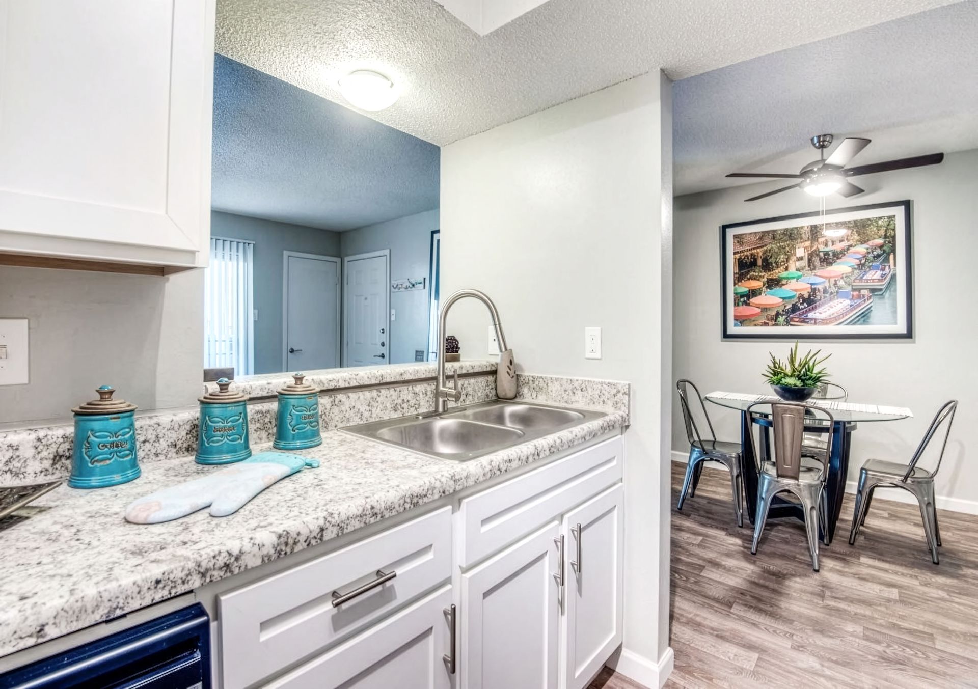 Bright kitchen with granite counters and sink opening to a small dining area with glass table and chairs