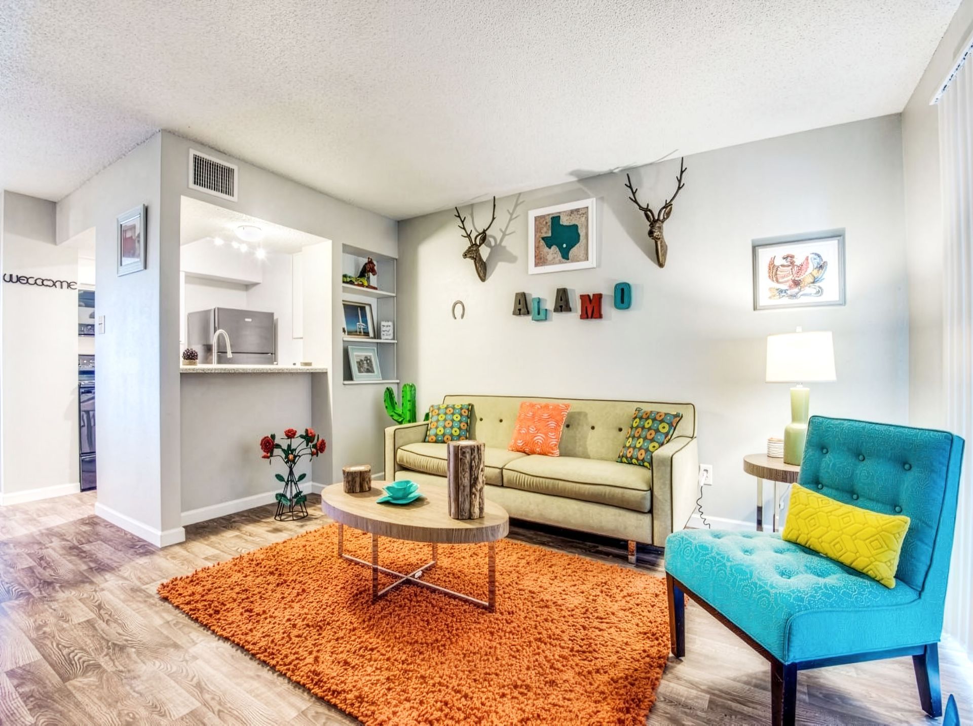 Bright living room with beige sofa, teal chair, orange rug, wall art, and a lamp