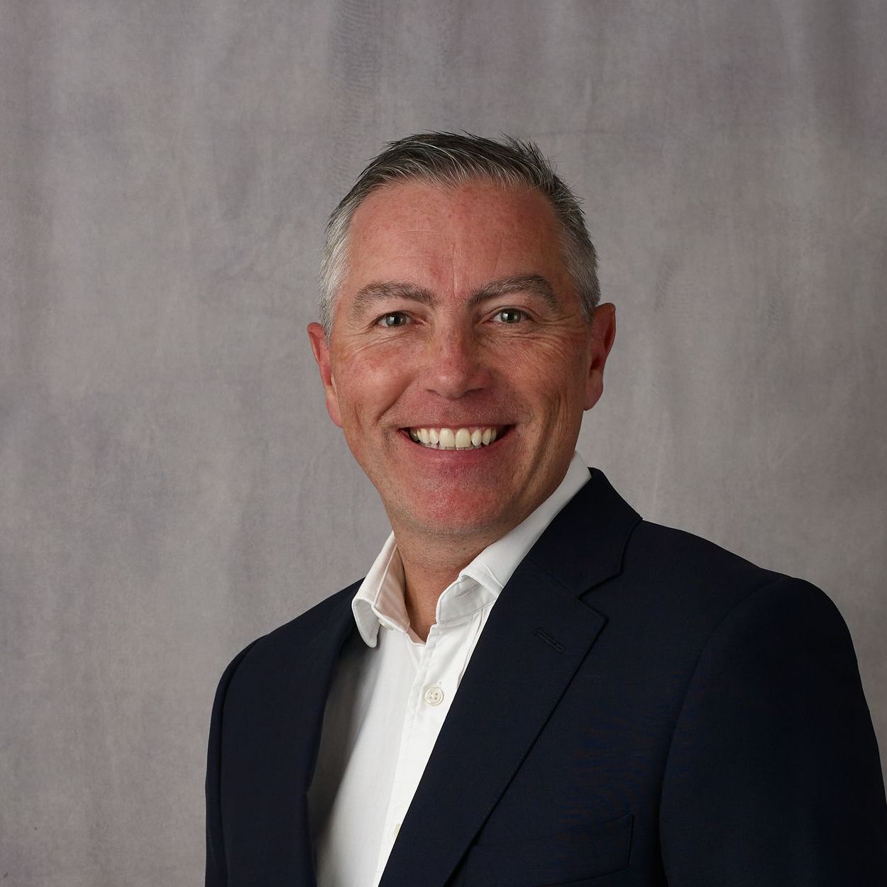 A man in a suit and white shirt is smiling for the camera.