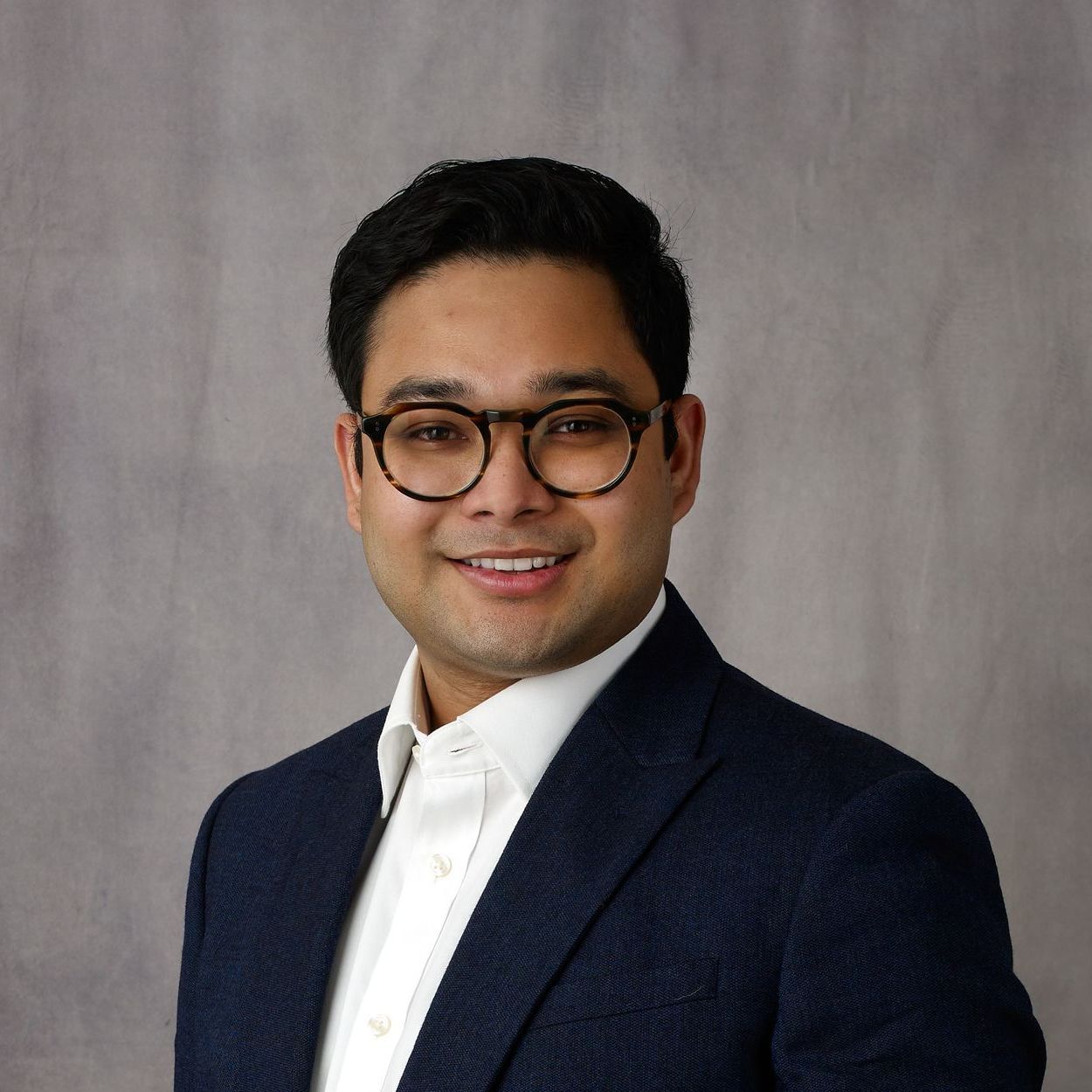 A man wearing glasses and a suit is smiling for the camera.