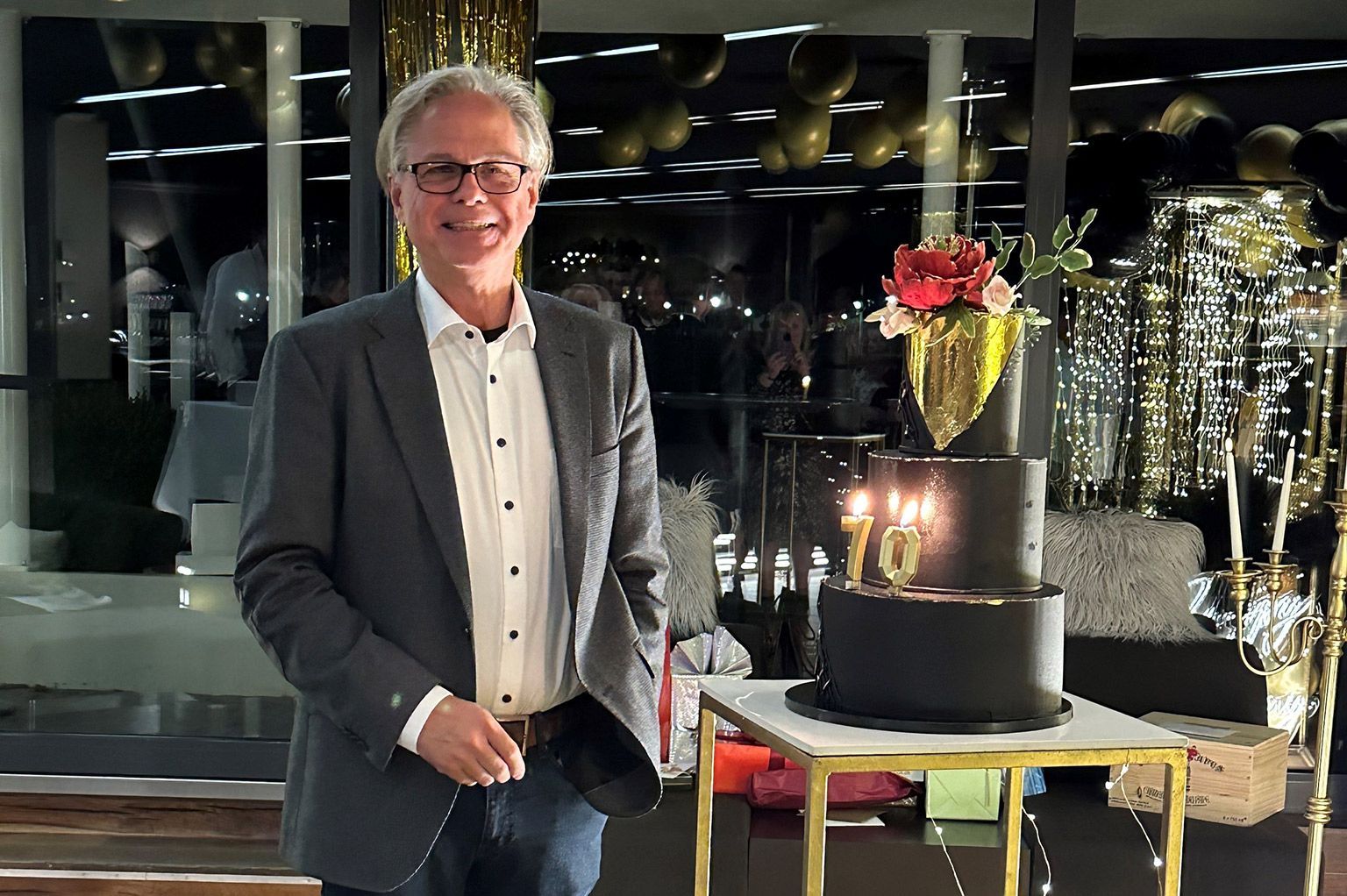 A man in a suit is standing in front of a black cake with candles on it.