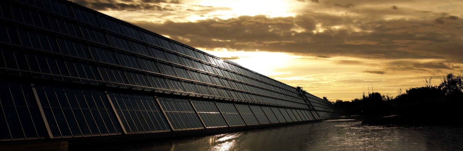 A row of solar panels against a cloudy sky at sunset.
