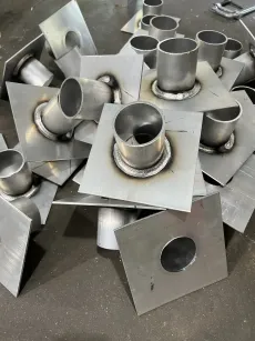 Scattered pile of welded metal parts: square plates with round tubes attached, possibly for plumbing or ventilation.