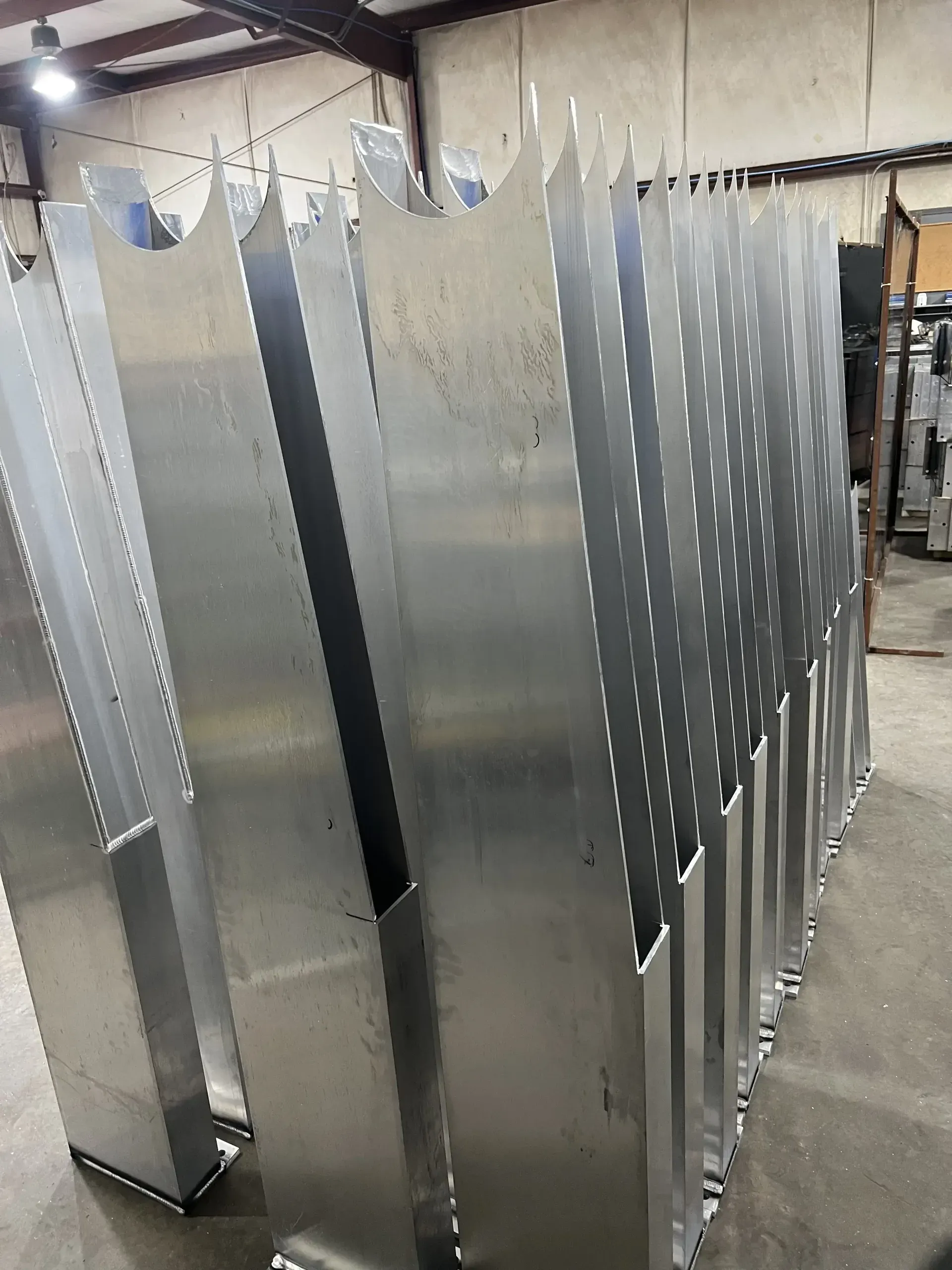 Metal industrial parts standing upright in a factory. Silver and geometric with cut-out designs.