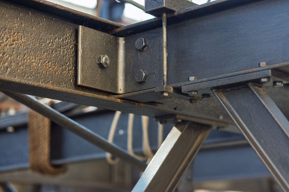 Close-up of a metal table base with bolts, brackets, and angled supports on a blue floor
