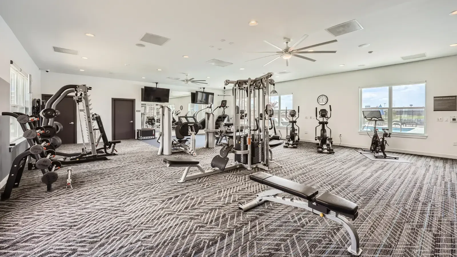 Interior view of a modern apartment gym with cardio machines, weight machines, and benches.