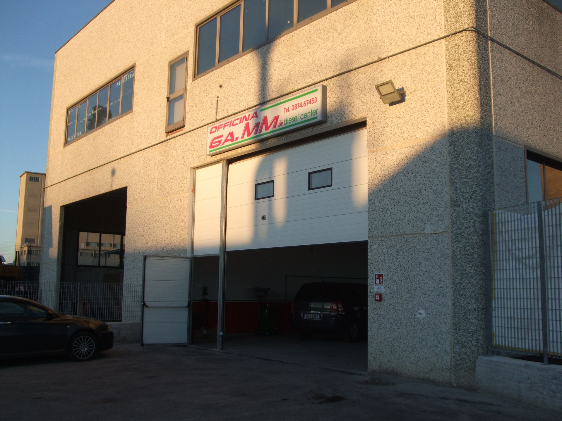 Esterno di un edificio industriale con porta del garage aperta. Il cartello sopra riporta la scritta 