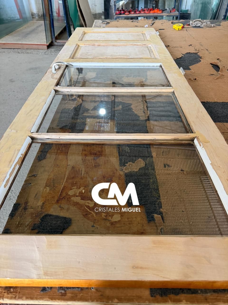 Puerta de madera con cristales, colocada plana sobre una superficie de trabajo, posiblemente para reparación o restauración.