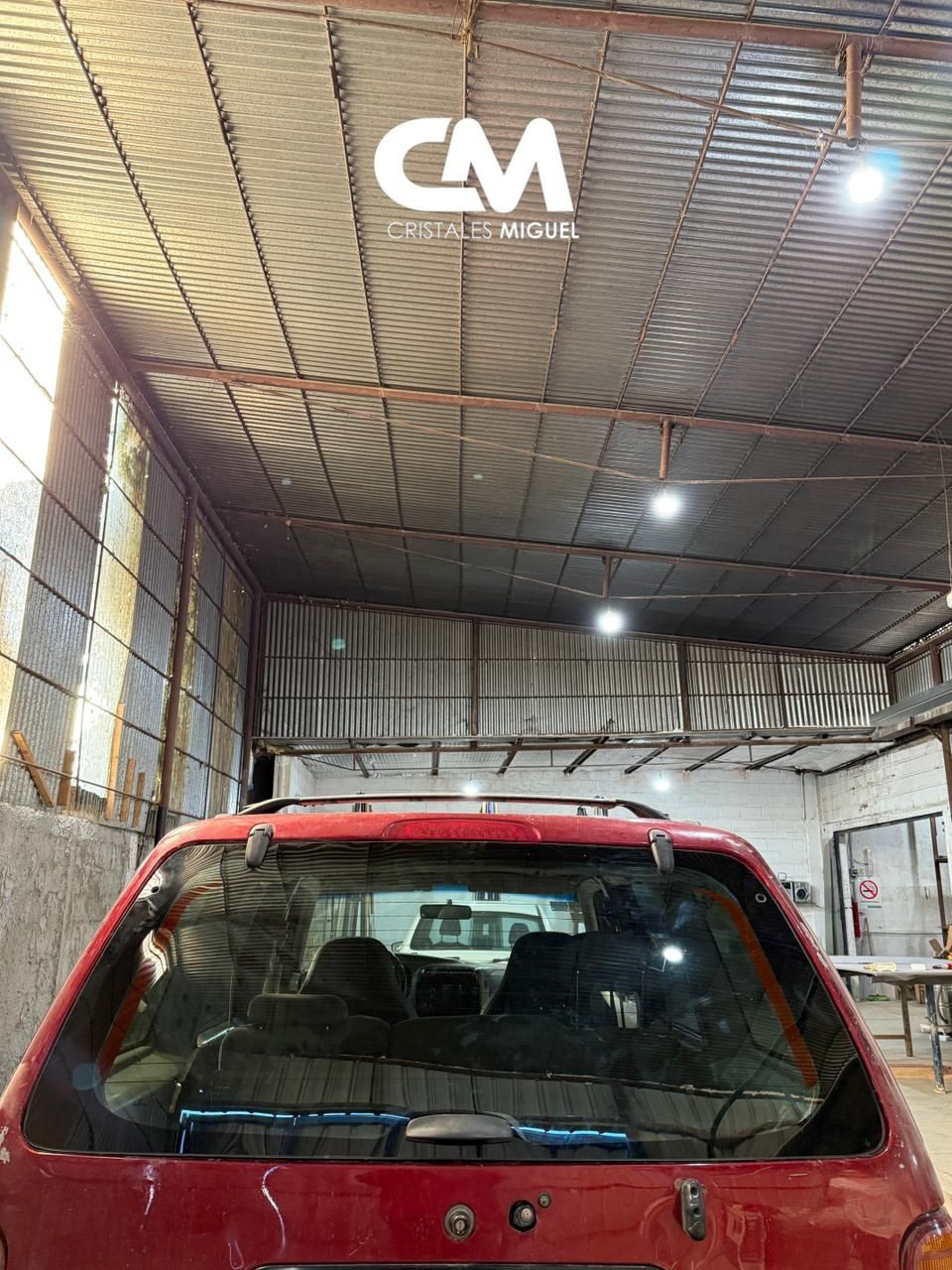 Coche rojo dentro de un taller. Techo de chapa ondulada y luces brillantes.