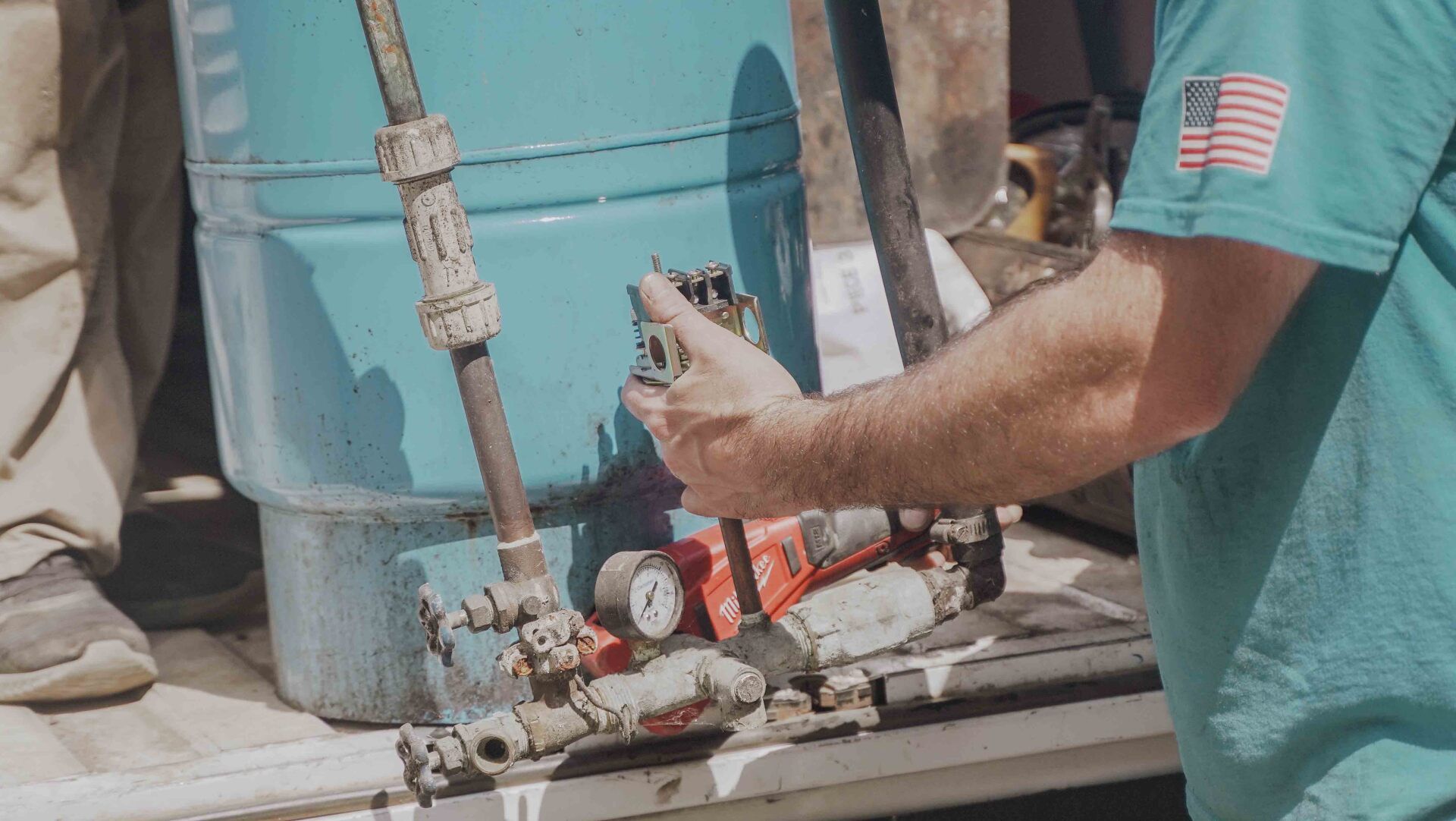 Worker holding a tool beside a large blue tank and red piping on a rooftop rooftop setup