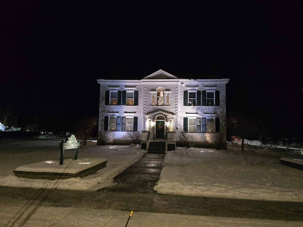 Snowy front yard with a lit stone house at night