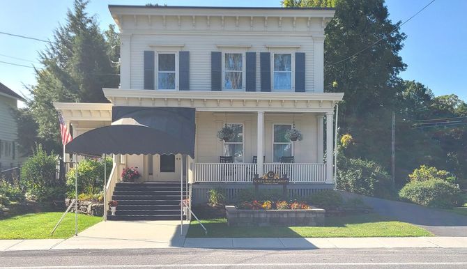 Two-story white house with blue shutters, front porch, and black awning, viewed from the street
