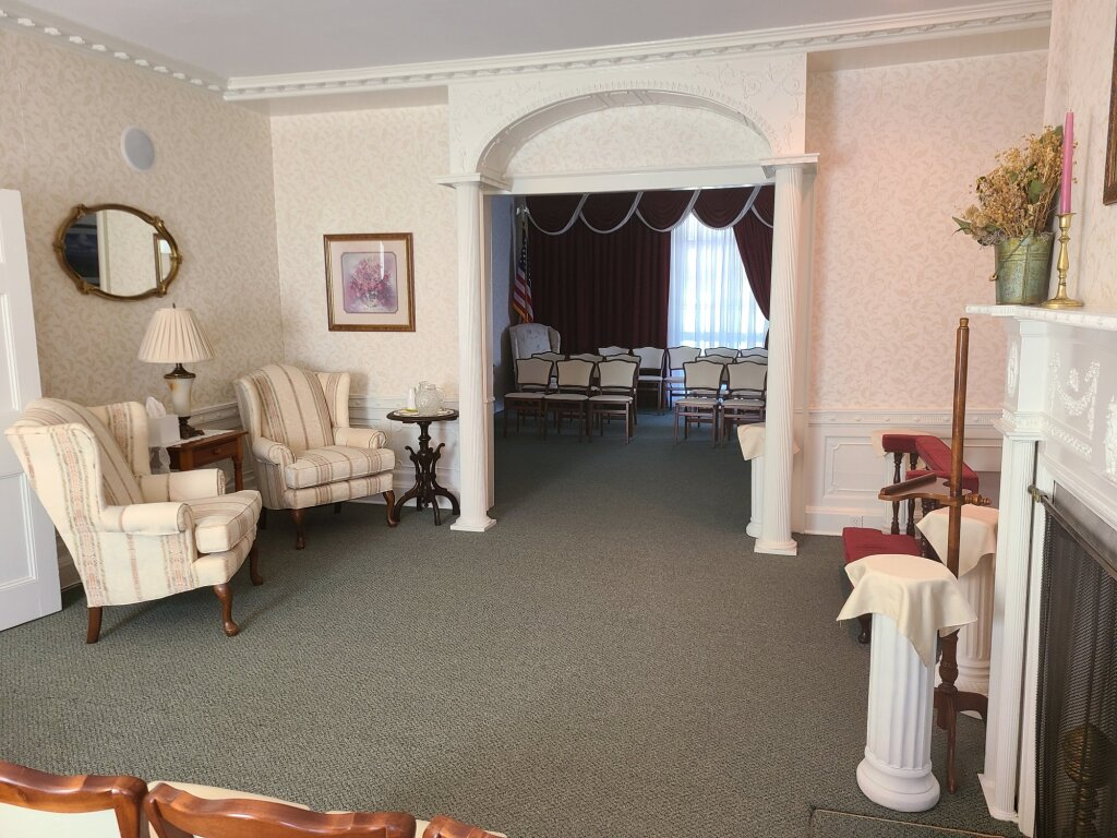 Elegant living room with cream walls, plaid chairs, fireplace, and arched doorway to a dining room.