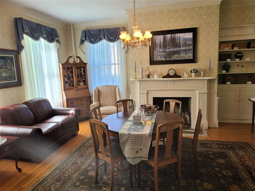 Cozy living room with leather sofa, fireplace, chandelier, dining table, and patterned rug