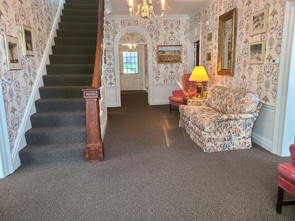 Floral wallpapered hallway with carpeted stairs, a patterned sofa, and a lit lamp in a cozy entryway.