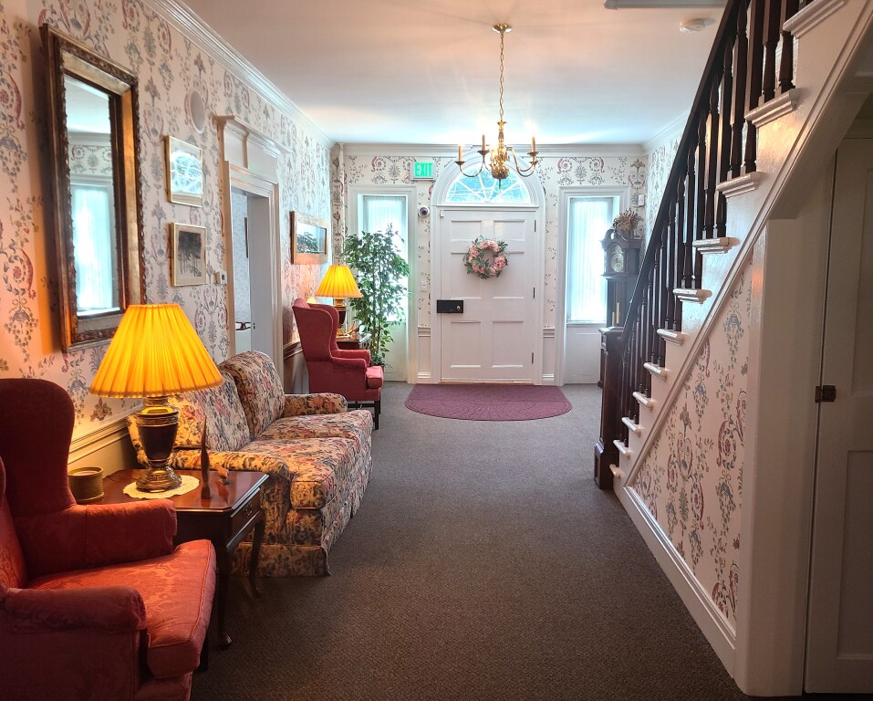 Cozy hallway with patterned wallpaper, red chairs, warm lamps, and a staircase on the right.