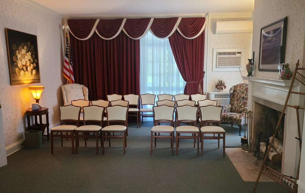 Empty meeting room with rows of chairs, red curtains, and a fireplace mantel on the right