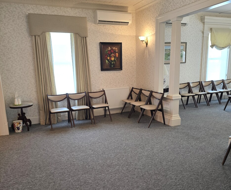 Quiet waiting room with gray carpet, folding chairs, wall art, and bright windows.
