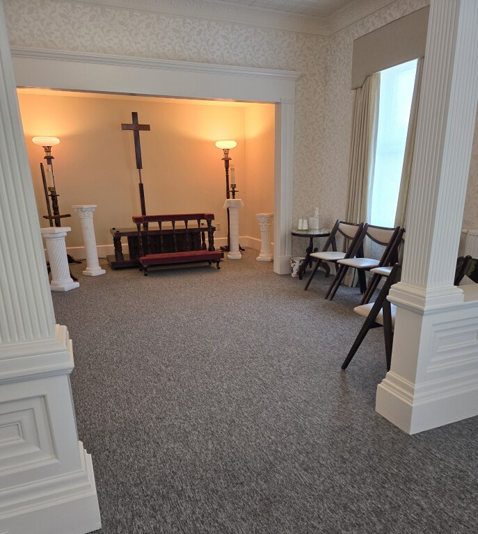 Small chapel with pews, a cross at the altar, and chairs along the side wall.