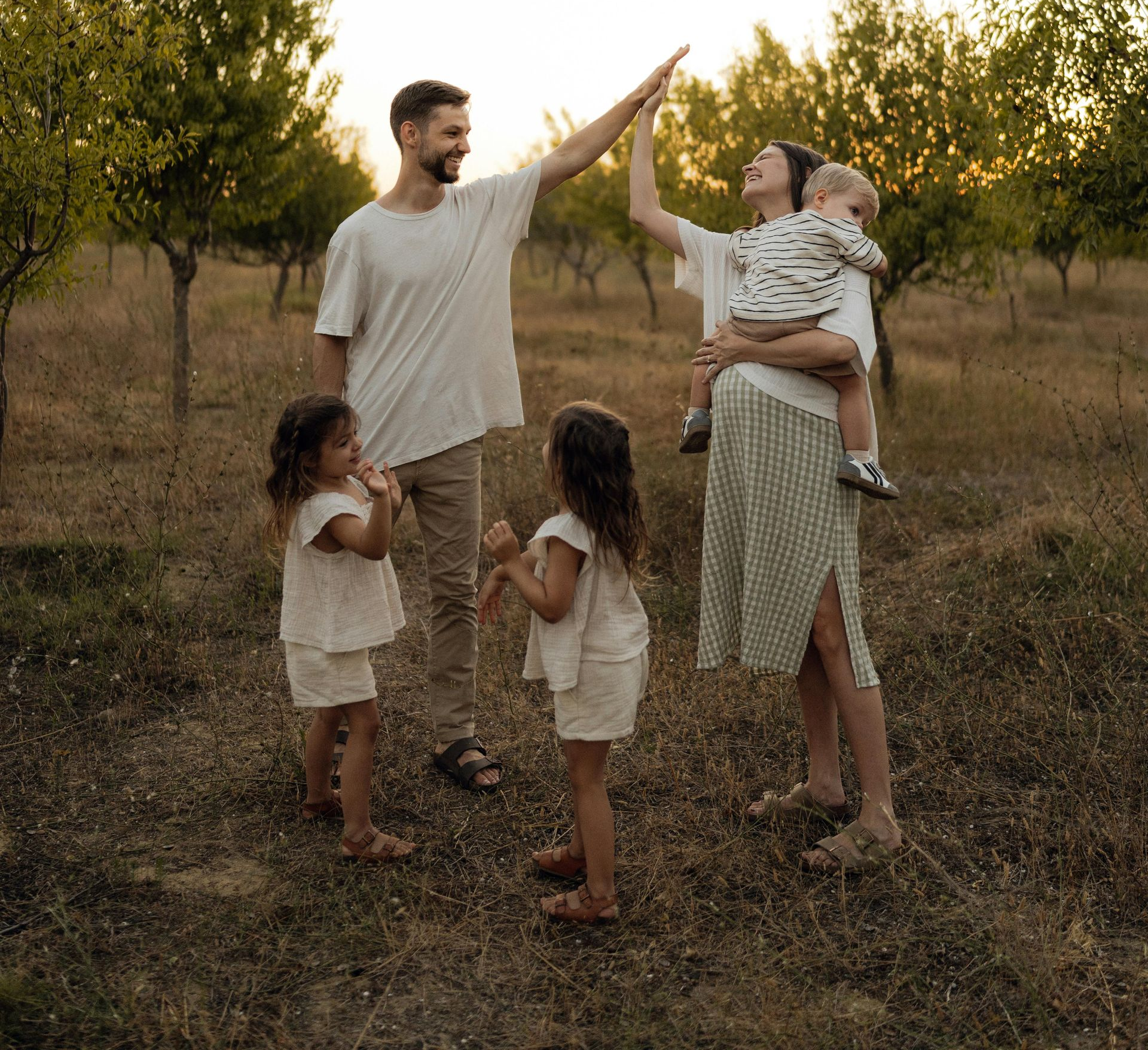 Family in a sunlit orchard, parents and children giving a high-five at dusk.