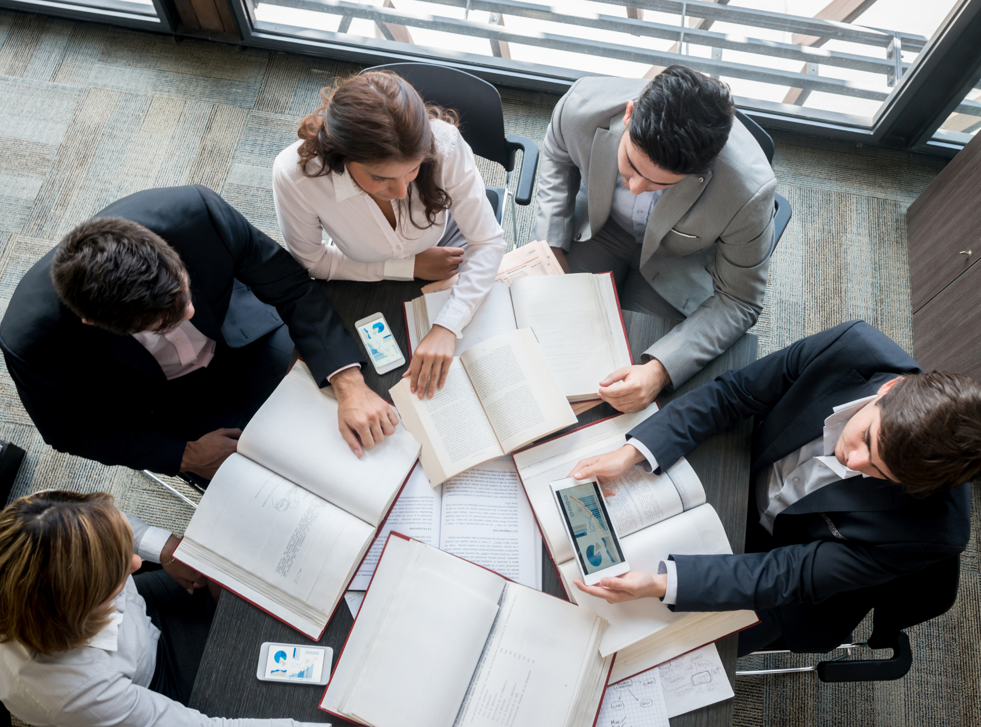 A group of people are sitting around a table with books and a tablet.