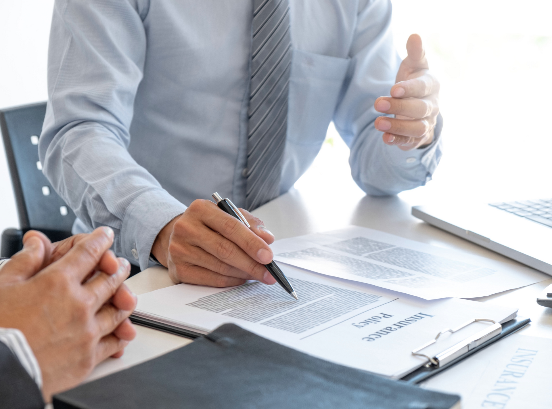A man is sitting at a table with a pen in his hand and talking to another man.