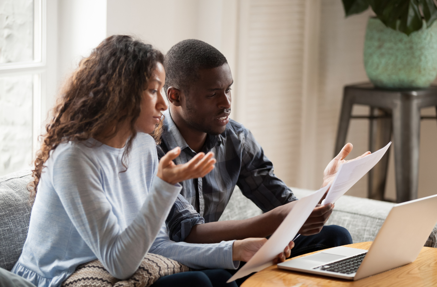 Two people reviewing documents at a table with a laptop in a bright living room